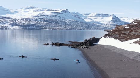 Kayakers-land-on-shore-of-remote-Holmanes-Peninsula-in-Reydarfjordur-fjord,-aerial