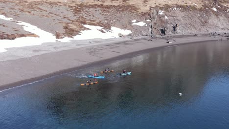 Kayakers-leaving-beach-in-Iceland-fjord-with-calm-clear-water,-Holmanes