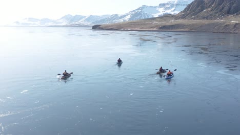 Following-four-kayakers-paddling-in-calm-flat-water-in-Iceland-Fjord,-aerial