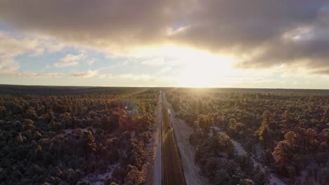 Beautiful-sunrise-aerial-as-car-passes-below-on-winter-forest-highway-sunrise,-4K