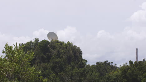 Satellite-Dish-Behind-Dense-Forest-Trees-In-Arecibo-Observatory-In-Arecibo,-Puerto-Rico-On-A-Sunny-Day