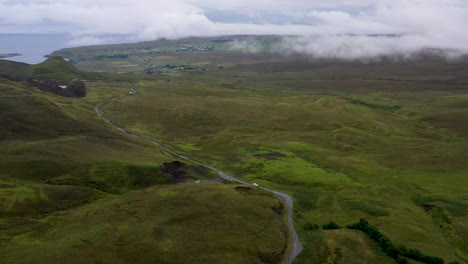 Wide-drone-shot-of-vehicle-on-road-near-Quiraing-the-landslip-on-the-eastern-face-of-Meall-na-Suiramach-in-Scotland