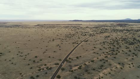 Wide-aerial-as-car-drives-down-highway-in-scrub-covered-desert-near-wupatki,-4K