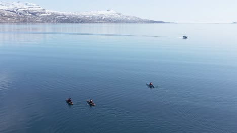 Vasto-Fiordo-Abierto-En-Islandia-Con-Kayakistas-De-Aventura-Remando-En-Aguas-Tranquilas,-Barco-Pasando,-Antena