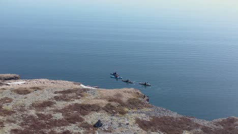 Kayakers-paddling-along-cliff-shore-of-Iceland-in-waveless-Fjord,-aerial