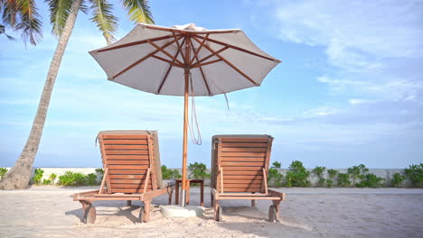 Two-empty-beach-loungers-under-a-shade-umbrella-face-out-at-an-ocean-view