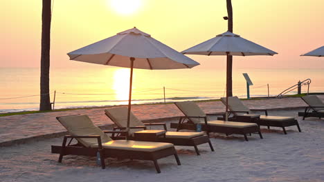 Seafront-lounge-on-the-beach-with-a-line-of-sunbeds-under-Parasols-at-golden-color-sunset-over-the-sea