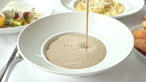 Pouring-mushroom-cream-soup-in-a-white-bowl-served-as-part-of-a-lunch-course-in-an-Italian-restaurant