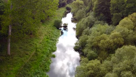 Aerial-close-shot-of-the-calm-stream-hidden-in-the-woods-with-clouds-reflecting-on-the-water---Little-Ouse-river-near-Thetford-in-the-UK