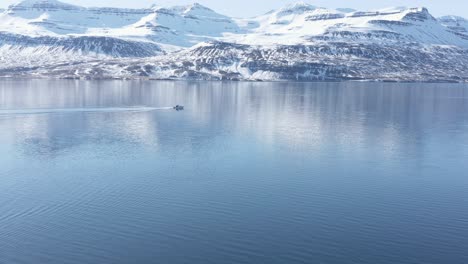 Boat-travels-through-fjord-in-Iceland,-snow-covered-mountains-in-background