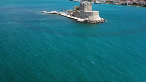 Flying-Over-Calm-Blue-Sea-Towards-Bourtzi-Castle-On-A-Sunny-Day-In-Nafplio,-Greece