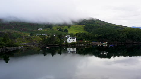 Rotating-drone-shot-of-a-fish-house-in-Loch-Carron-with-low-lying-clouds-covering-the-mountains,-in-the-Scottish-Highlands