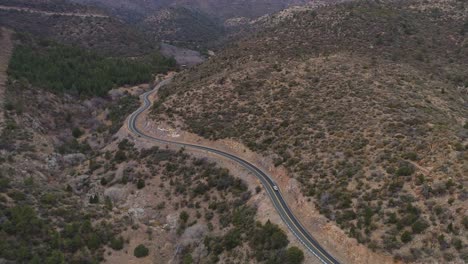 Aerial-following-vehicle-on-winding-highway-through-arid-mountains,-4K