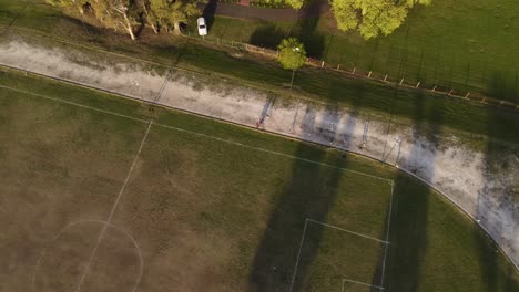 Luftaufnahme-Von-Oben-Nach-Unten-Von-Kindern,-Die-Bei-Sonnenuntergang-Auf-Einem-Fußballplatz-Laufen-Und-Trainieren
