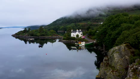 Drone-shot-of-starting-on-a-fish-house-slowly-revealing-Loch-Carron-with-low-lying-clouds,-in-the-Scottish-Highlands