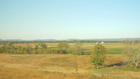 Beautiful-scenic-view-of-grasslands-covered-with-yellow-and-green-grass-and-a-forest-and-cottages-at-a-distance-on-a-bright-sunny-day-near-the-Civil-War-battlefields-near-Gettysburg,-PA-USA