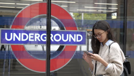 Stylish-young-professional-woman-waiting-outside-London-Underground-station-using-her-smart-phone