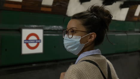 Woman-wearing-a-face-mask-is-waiting-for-a-tube-train-in-a-London-underground-station