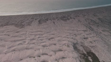 Aerial-flying-over-sand-beach-by-sea-in-evening,-no-people