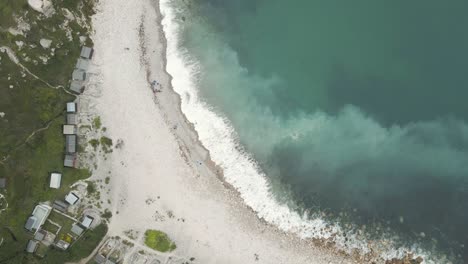 Aerial-shot-of-a-drone-flying-high-in-the-sky,-facing-down-on-the-waves-hitting-the-beach-of-Church-Ope,-on-the-island-of-Portland,-in-Dorset-UK