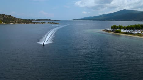 4K-Drone-clip-slowly-moving-backwards-with-jetski-approaching-in-the-bay-of-Vourvourou,-in-Chalkidiki,-northern-Greece