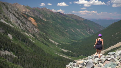 Young-Female-Hiker-WIth-Helmet-Walking-on-Rocky-Boulder-WIth-Stunning-View-of-Green-Valley-in-Rocky-Mountains,-Colorado-USA