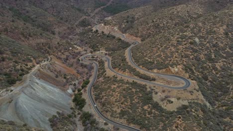 Aerial-panning-down-to-car-traveling-barren-mountain-road-with-switchbacks,-4K