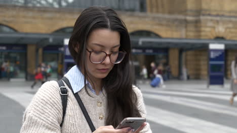 Beautiful-Asian-American-Woman-stood-outside-Kings-Cross-Station,-London-using-her-smartphone