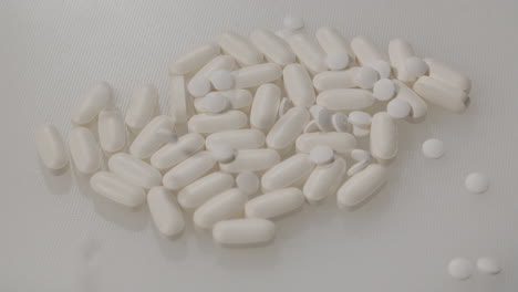 Small-white-pills-falling-on-pile-of-pills-on-a-white-surface