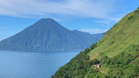 Timelapse-of-Central-American-volcano-Volcan-San-Pedro-in-Lake-Atitlan,-Guatemala-on-a-sunny-day-with-boat-traffic-over-the-blue-lake-water-and-Santa-Cruz-La-Laguna-green-hillside-in-the-foreground
