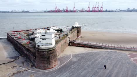 Fort-Perch-Rock-New-Brighton-sandstone-coastal-defence-battery-museum-and-Peel-port-cranes-aerial-view-orbit-right