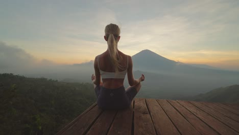 Behind-fit-blond-woman-sitting-in-easy-lotus-pose-with-silhouette-of-Mount-Agung