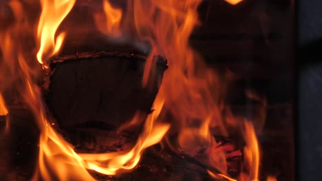 Up-close-shot-of-traditional-household-wood-fire-burning-large-piece-of-timber-with-red-hot-orange-flames-flickering-in-slow-motion