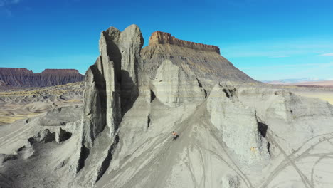 Aerial-View-of-Man-Running-Down-the-Hill,-Grey-Sandstone-Formation-in-a-Front-of-Factory-Butte,-Utah-Desert-USA