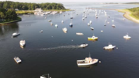 Small-Boat-Sailing-At-Cohasset-Harbor,-Massachusetts-With-Many-Boats-Docked-On-Water-Surface