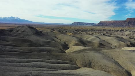 Aerial-View-of-Man-Running-on-Barren-Dry-Badlands,-Desert-Landscape-of-Utah-USA