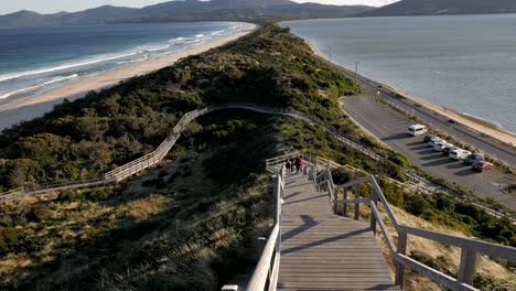 Slow-pan-up-over-neck-isthmus-wooden-timber-boardwalk-on-Bruny-Island-Tasmania-Australia-during-breezy-spring-evening-with-waves-rolling-in-background-coastline-forest-mountain