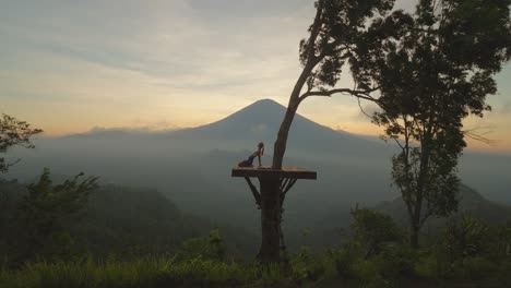Woman-bending-backwards-in-camel-pose-on-wooden-platform-with-magical-view-of-Mount-Agung,-moment-of-zen