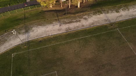 Luftaufnahme-Von-Oben-Nach-Unten-Der-Einzigen-Person,-Die-Bei-Sonnenuntergang-Auf-Einem-Fußballplatz-Trainiert