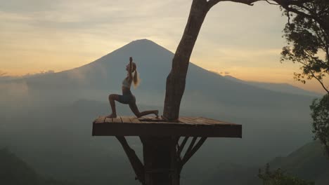 Woman-practicing-warrior-pose-on-wooden-platform-with-Mount-Agung-in-Background