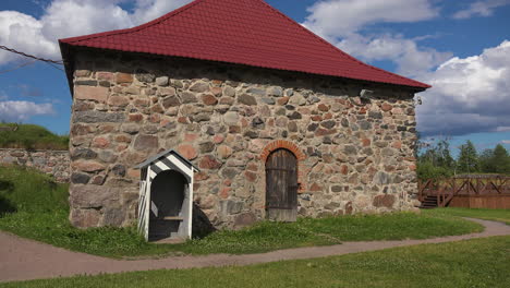 An-outside-view-of-a-hall-of-an-old-fortress-made-of-stones-with-a-small-gate,-red-tiles-top,-Russia