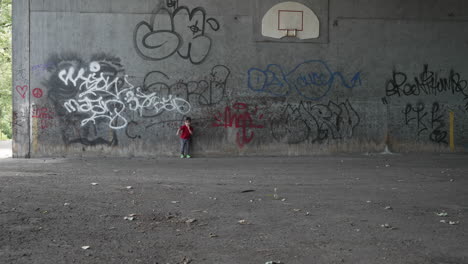 Zeitlupenvideo-Eines-Kleinen-Jungen-In-Einem-Roten-T-Shirt,-Der-Sich-An-Eine-Graffitiwand-Lehnt-Und-Auf-Die-Kamera-Zuläuft