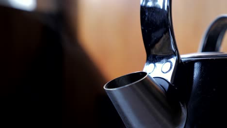 Tight-up-close-shot-of-black-household-domestic-kitchen-kettle-slowly-boils-for-cup-of-tea-coffee-with-steam-water-vapor-coming-out-of-metal-spout