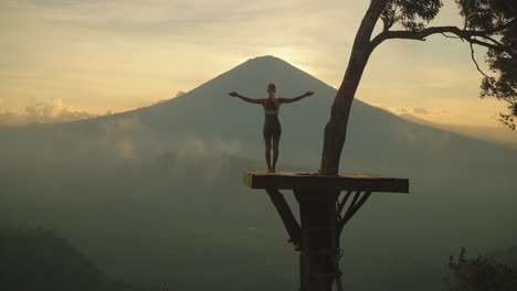 Woman-stretching-and-extending-arms-while-looking-at-Mount-Agung-during-sunset,-Lahangan-Sweet