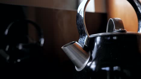Fixed-shot-of-black-household-domestic-kitchen-kettle-slowly-boils-for-cup-of-tea-coffee-with-steam-water-vapor-coming-out-of-metal-spout
