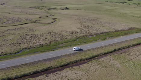 Car-travels-along-scenic-route-in-open-grass-land-of-Iceland,-Aerial