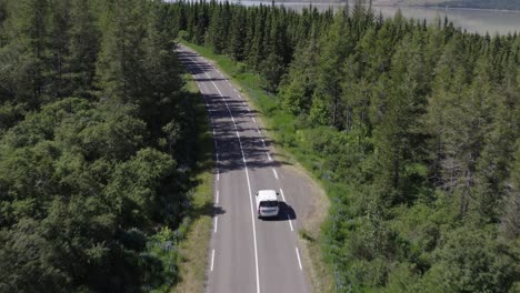 Evergreen-forest-in-Iceland-with-white-car-driving-on-remote-road,-aerial