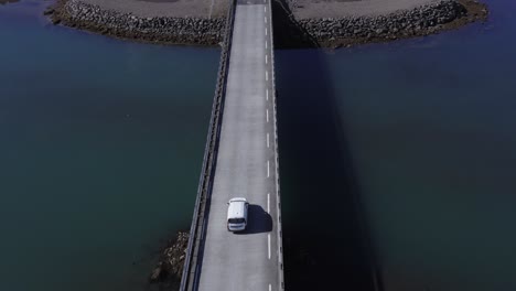 White-car-crossing-bridge-over-calm-river-mouth-at-Iceland-coastal-land,-aerial