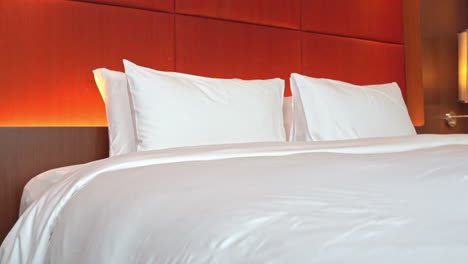 Close-up-Pan-of-a-large-hotel-bed-with-an-orange-colored-headboard