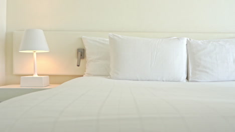 Modern-hotel-room-interior---panning-left-on-white-bed-for-two-person-with-4-pillows,-king's-size-bed-and-white-night-lapm-standing-on-cabinet